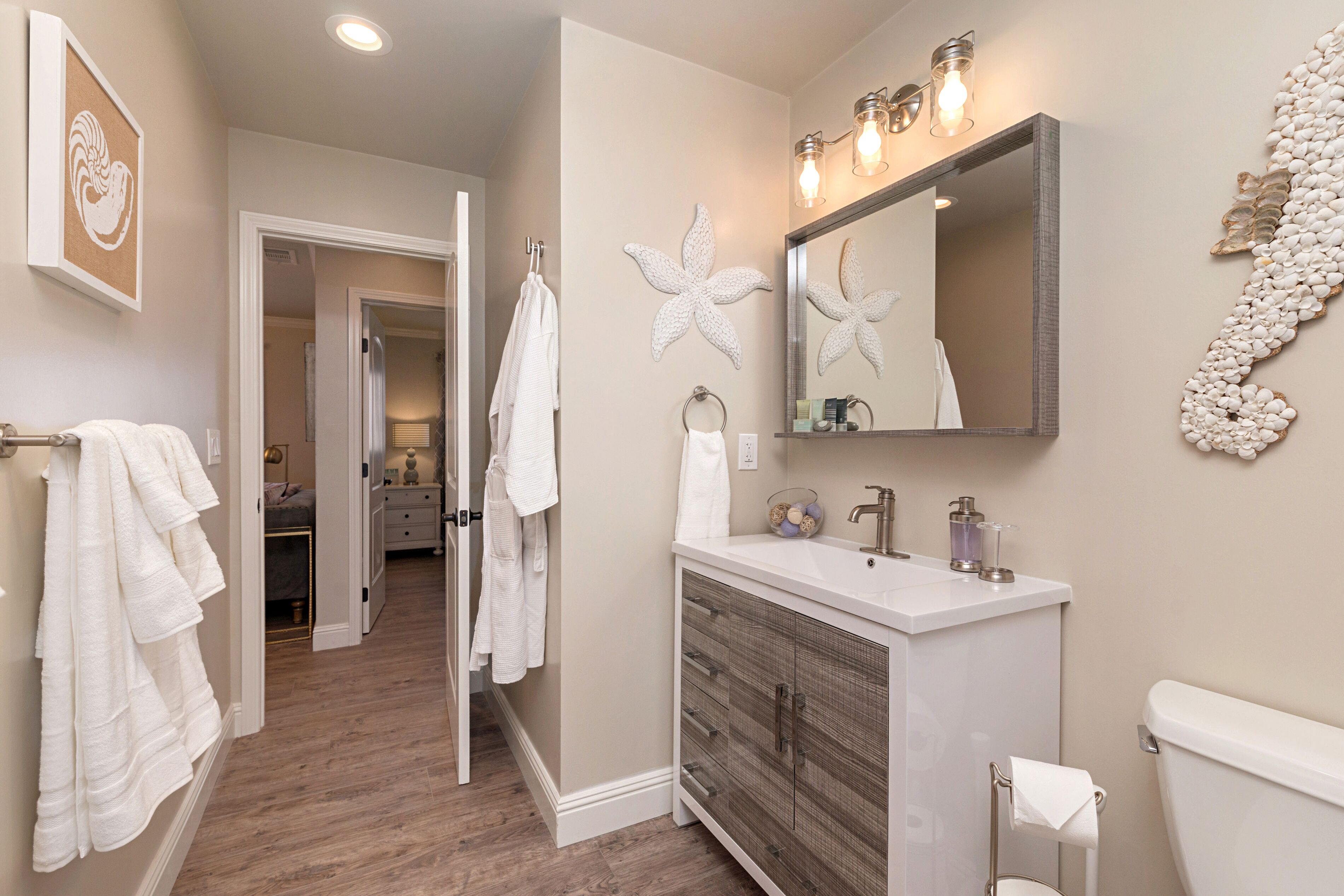 Un bagno con un mobile lavabo bianco, uno specchio grande e un water. Asciugamani su un portasciuga e un elemento decorativo a parete.