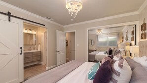 Ein Schlafzimmer mit einem großen Bett, einer Chandelier, ein Badezimmer mit einem Spiegel und einem Flur zu einem weiteren Raum.