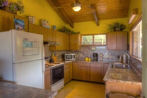 A compact kitchen with wooden cabinets, a refrigerator, a microwave, a stove, and a sink.