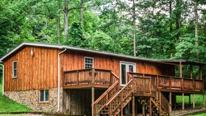 Une cabane en bois avec des fondations en pierre, une terrasse en bois et un escalier menant à un deuxième étage.