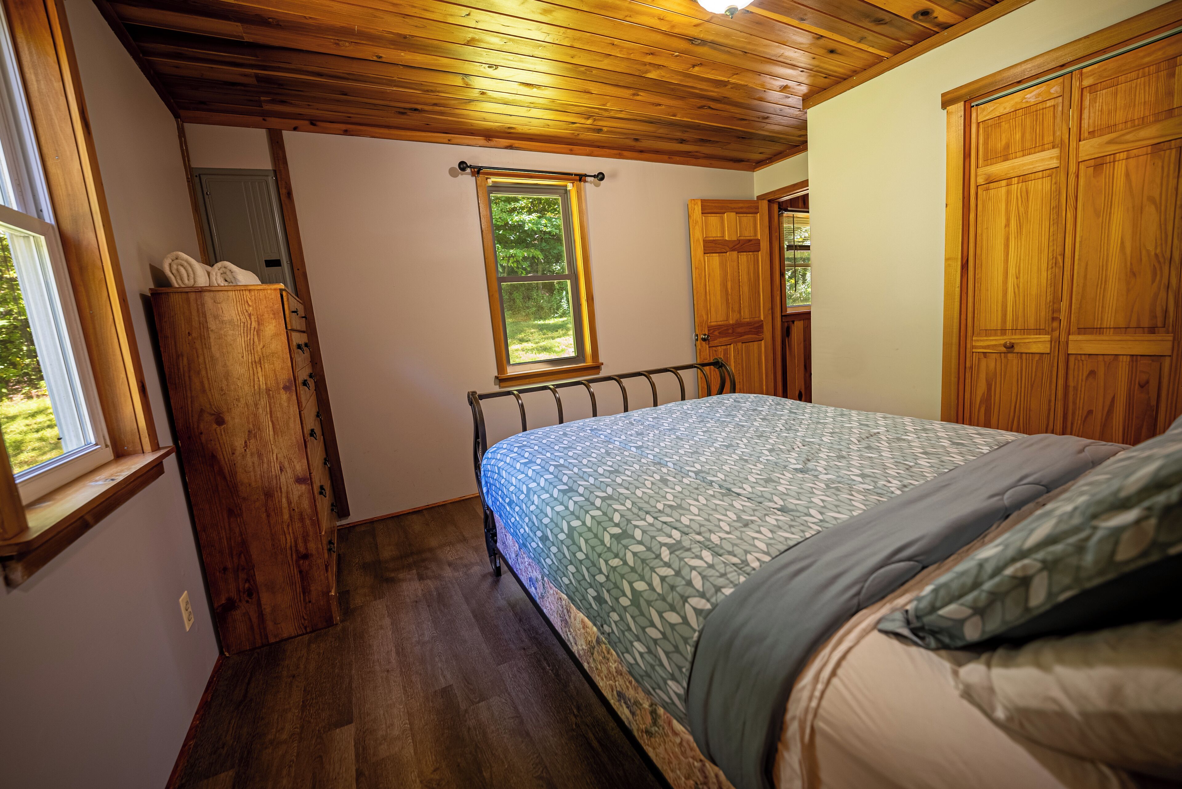 A bedroom with a bed, wooden wardrobe, and a window with a view of greenery.