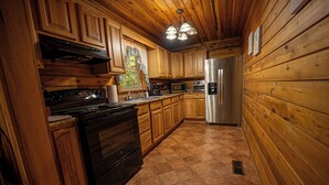 Une cuisine rustique, située dans une cabane en bois, équipée d’une cuisinière, d’un four, d’un four à micro-ondes, d’un réfrigérateur et de meubles de rangement en bois.