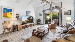 Una sala de estar amplia con ventilador de techo, un ventanal grande, un sofá, una mesa de centro y un televisor.