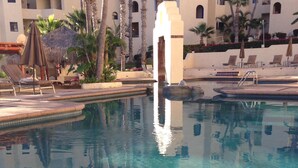 Ein Swimmingpool mit klarem Wasser, umgeben von Liegestühlen und Palmen, mit einem Gebäude im Hintergrund.