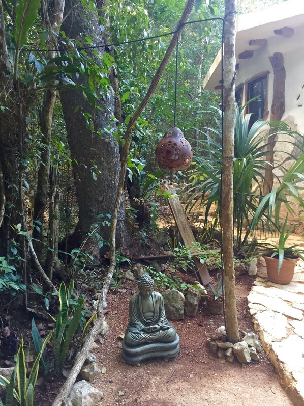 A serene garden with a Buddha statue, lush greenery, and a hanging decorative pot.