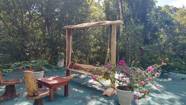 A wooden swing set in a garden with potted plants and rustic furniture.