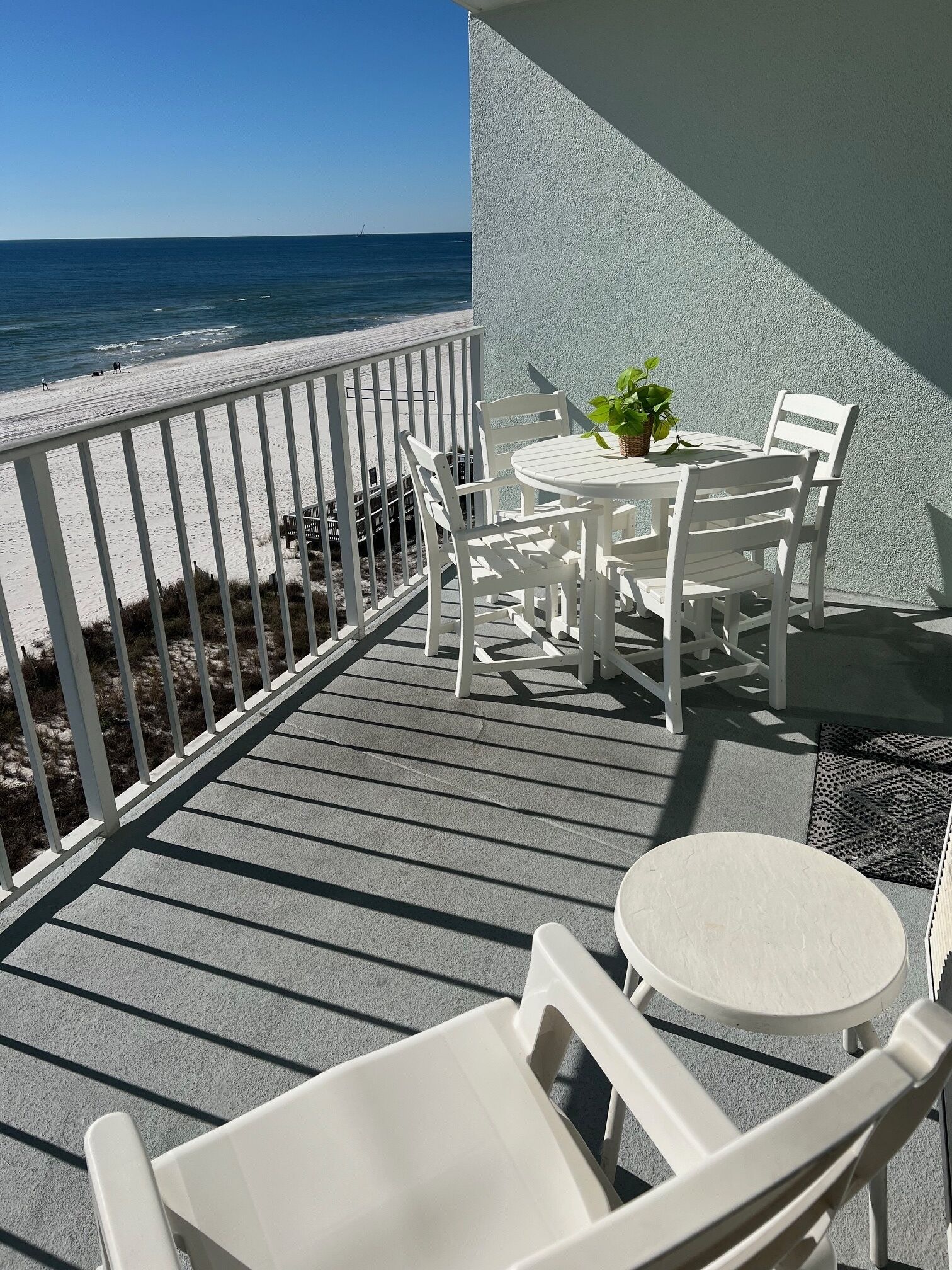 Ein Balkon mit Blick auf den Strand, weiße Gartenmöbel und ein kleiner Tisch mit einer Pflanze.