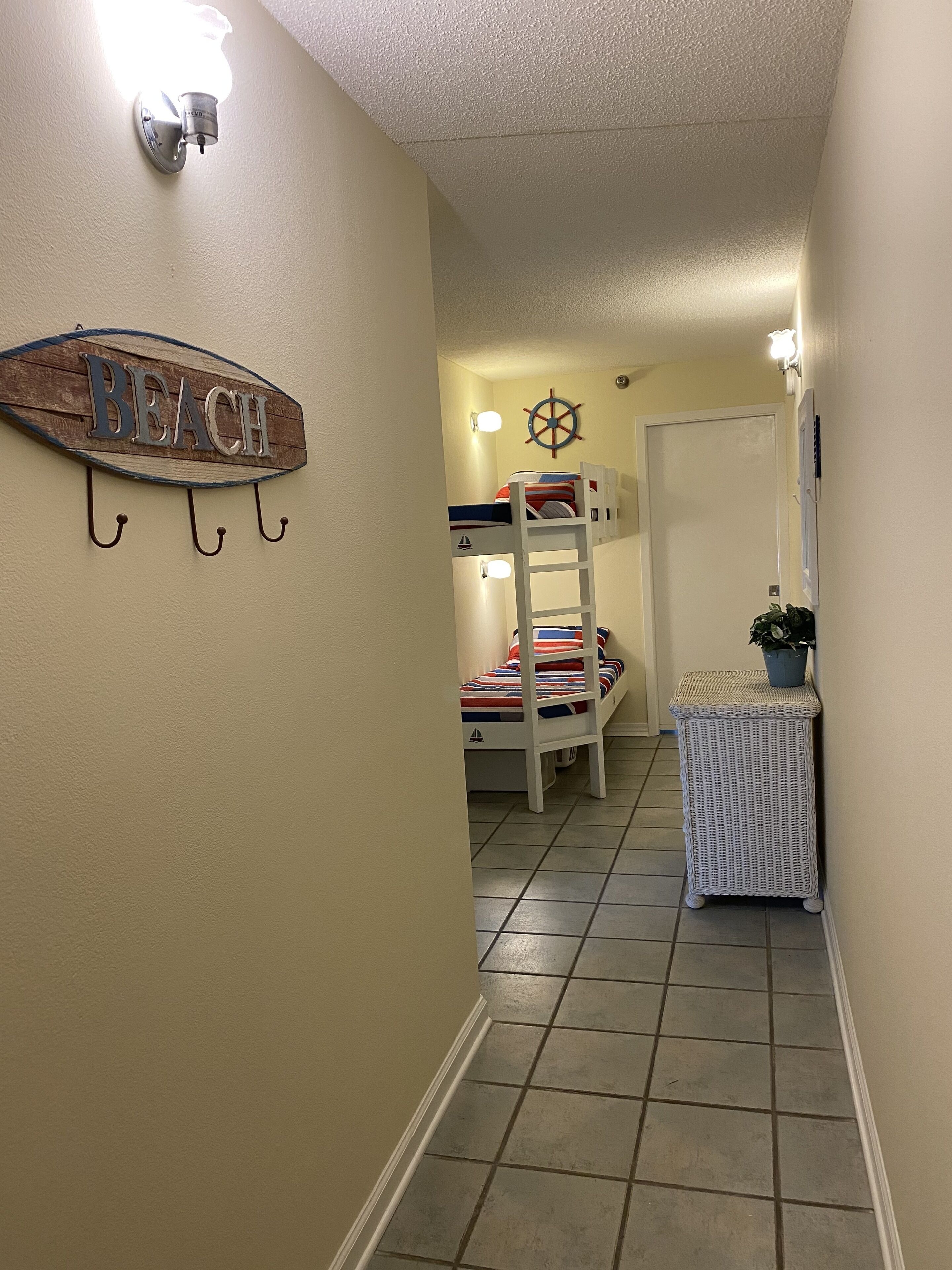 A hallway with a bunk bed, a small table with a plant, and a wall-mounted sign reading "BEACH".