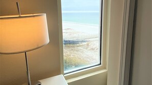 A room with a window overlooking a beach, a lamp on a desk, and a wooden floor. - Save 10% Last min & Week! Gulf Front, Panoramic Views, Beach Supplies, Pool! (Orange Beach)