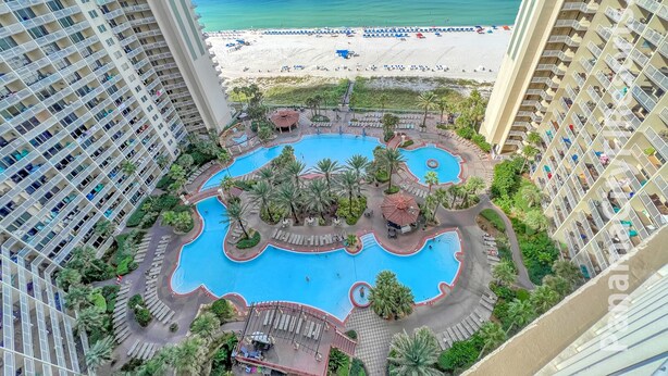 A high-rise hotel with a central swimming pool surrounded by palm trees and lounge areas, overlooking a beach. - Less Crowds More Paradise! Enjoy Sea View at the Shores of Panama  2 br, 2 bath (Panama City Beach)