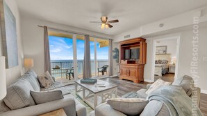 A spacious living room with a balcony, a wooden TV stand, and a dining area. - Less Crowds More Paradise! Enjoy Sea View at the Shores of Panama  2 br, 2 bath (Panama City Beach)