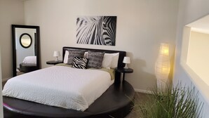 A modern bedroom with a large bed, a round mirror, a zebra-patterned wall art, and a bedside lamp. - Clean & Cozy Condo with pool and trailer parking! (Mesquite)