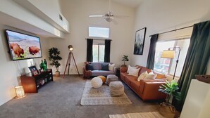 A spacious living room with a large flat-screen TV, a sofa set, a coffee table, and a floor lamp. - Clean & Cozy Condo with pool and trailer parking! (Mesquite)