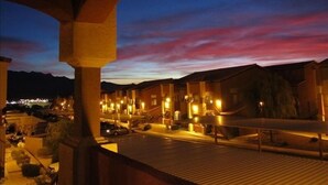 A hotel with a row of uniformly styled buildings, a covered outdoor area with a wooden deck, and a view of the mountains in the background. - Clean & Cozy Condo with pool and trailer parking! (Mesquite)