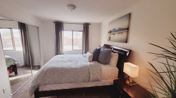 Een net opgemaakt bed met een gebloemd kleed, een bedlampje en een schilderij aan de muur.