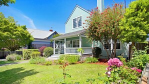 A house with a front porch, surrounded by a well-maintained garden with various plants and flowers. - Walk to Downtown from this Spacious Home (Napa)