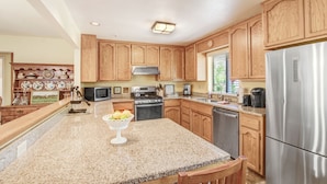 A kitchen with wooden cabinets, granite countertops, a stainless steel refrigerator, and a microwave. - Walk to Downtown from this Spacious Home (Napa)