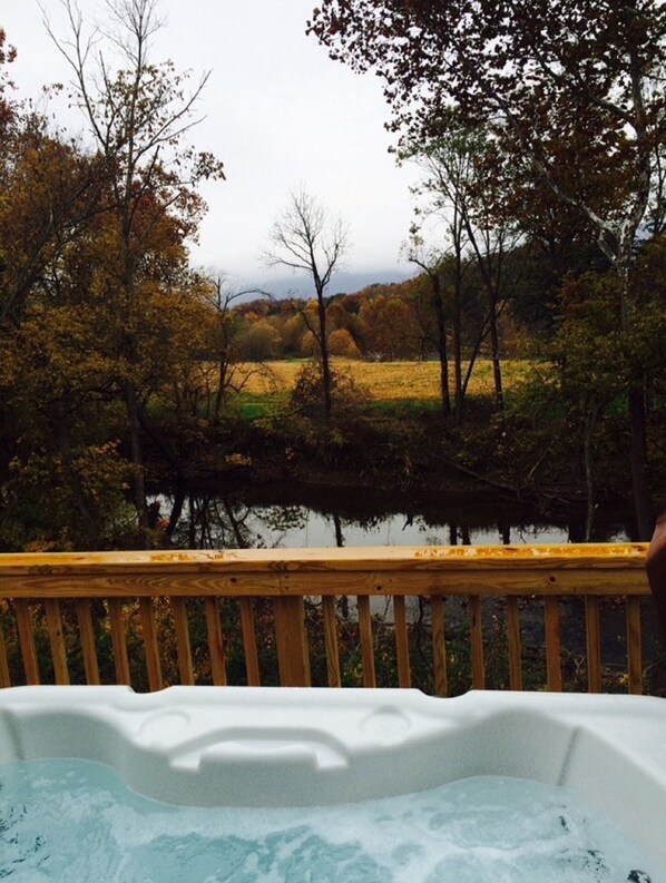 A hot tub with a wooden deck overlooking a lake surrounded by autumn trees. - Beautiful River Front Cabin with Mountain views (Luray)