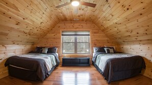Un dormitorio acogedor en el ático, con paredes de madera, techo inclinado y un ventanal grande.