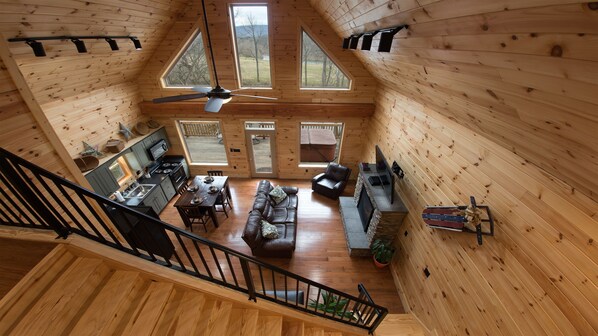 A spacious cabin with a high ceiling, wooden walls, a dining area, a living room, and a kitchen. - Beautiful River Front Cabin with Mountain views (Luray)