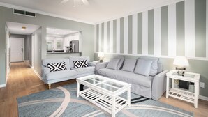 A modern living room with a grey sofa, a glass coffee table, and striped wallpaper. - Golf cart, newly renovated villa, pet friendly! (Destin)