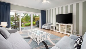A living room with a sofa, coffee table, TV, and a view of the outdoors. - Golf cart, newly renovated villa, pet friendly! (Destin)