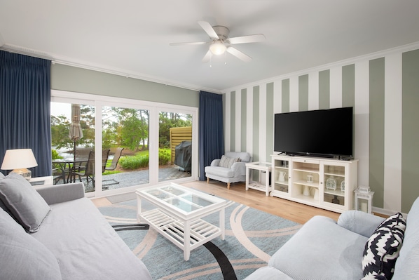 A living room with a sofa, coffee table, TV, and a view of the outdoors. - Golf cart, newly renovated villa, pet friendly! (Destin)