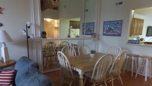 A dining area with a wooden table and chairs, a blue sofa with American flag pillows, and a kitchen in the background. - Updated with everything you need for family fun time, just minutes to beach! (Ocean View)