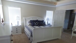 A bedroom with a large bed, two bedside tables, a dresser, and a door leading to another room. - Updated with everything you need for family fun time, just minutes to beach! (Ocean View)