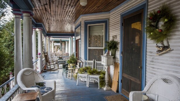 A covered porch with wicker furniture, a wooden ceiling, and a Christmas wreath.