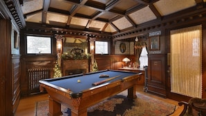 A billiards room with a pool table, wooden paneling, a radiator, and a Christmas tree.