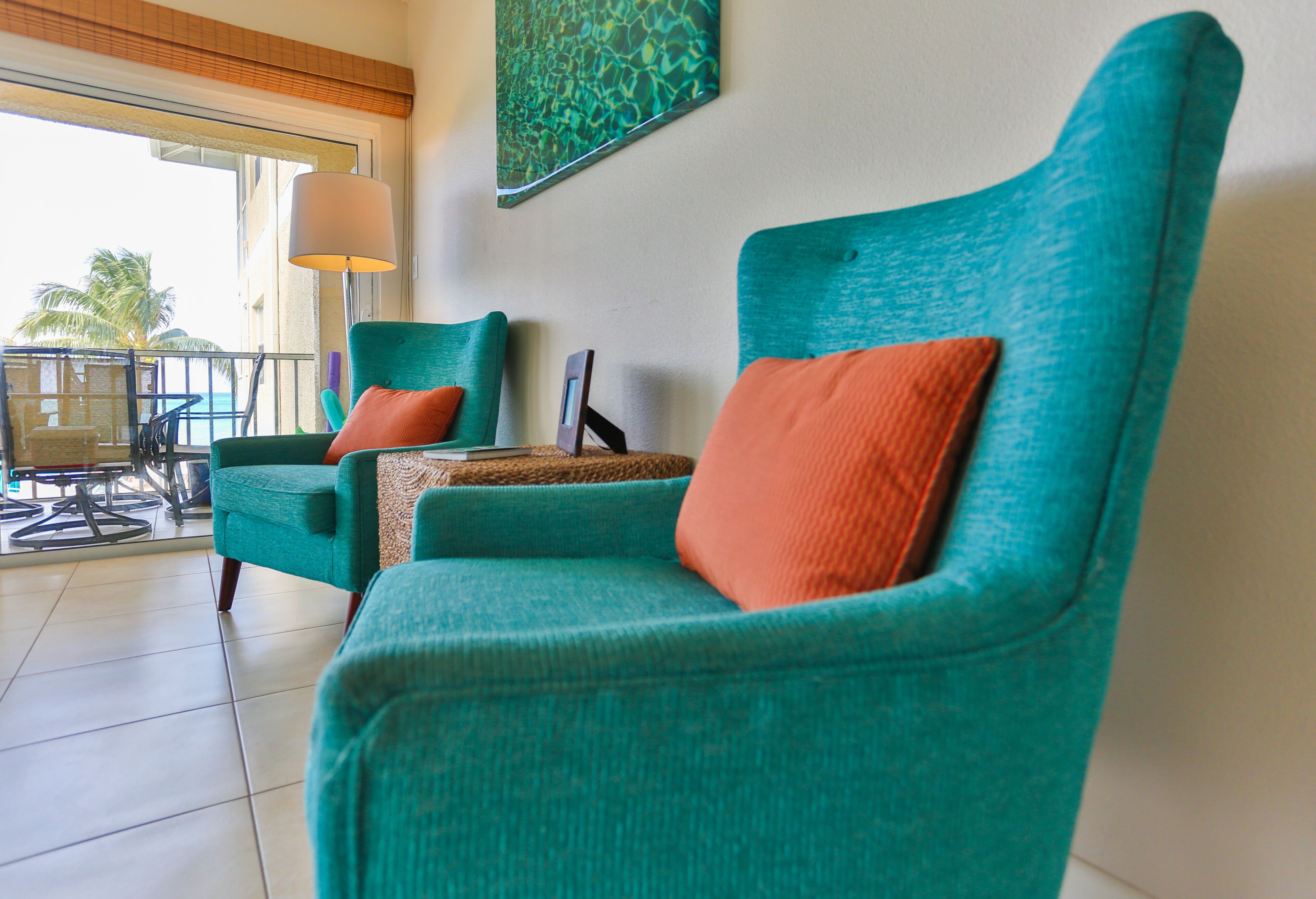 A room with teal armchairs, a small table, and a view of the ocean.