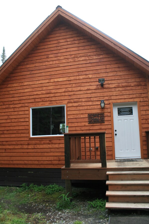 A wooden cabin with a white door, a small window, and a wooden deck.
