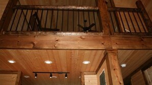 A wooden balcony with a railing, wooden beams, and recessed lighting.