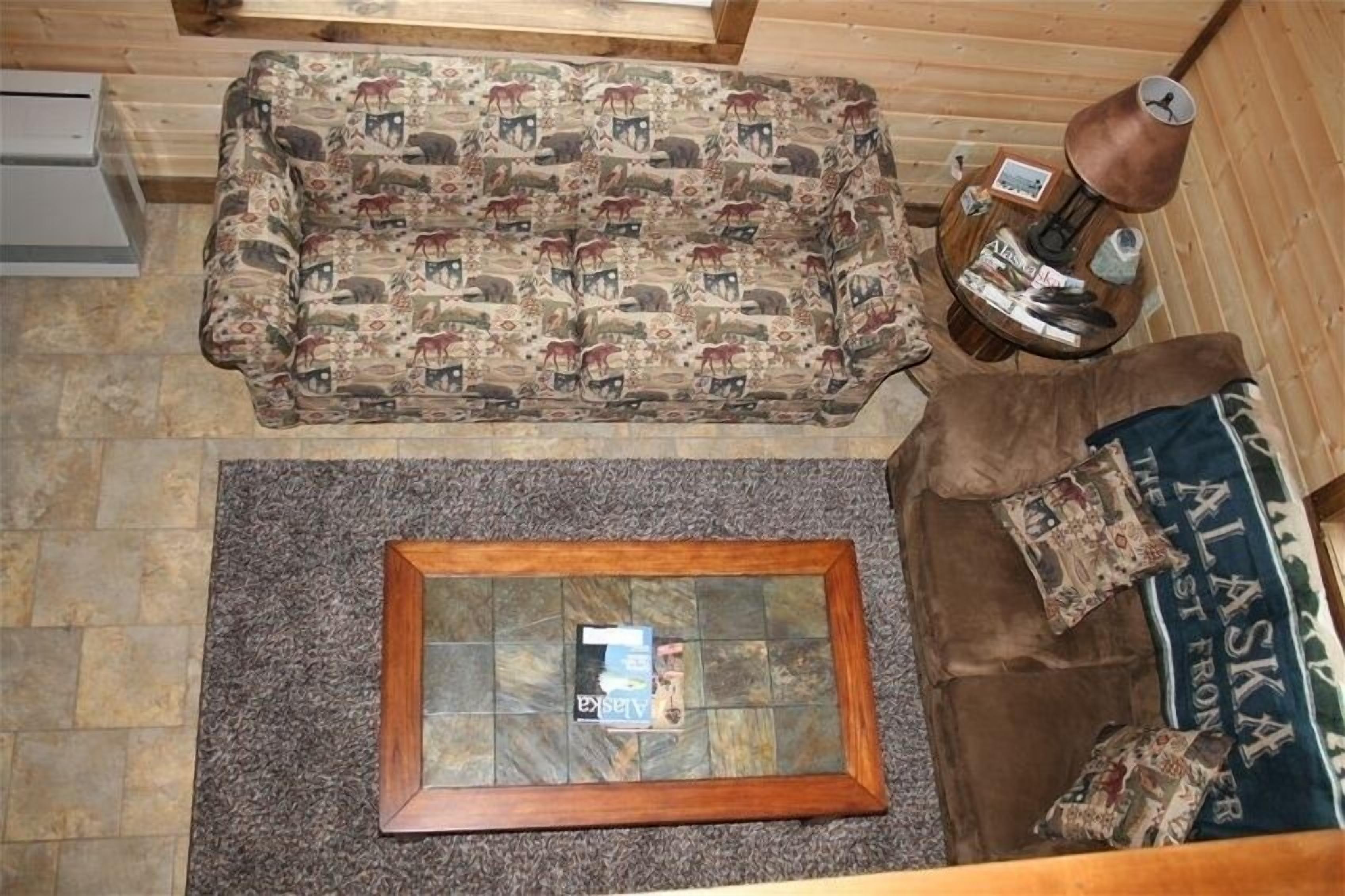 Una habitación acogedora con un sofá estampado, una mesa de centro de vidrio y un sofá de cuero con almohadones alusivos a Alaska.