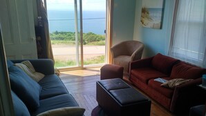 A living room with a blue sofa, a red sofa, and a brown armchair. There is a large window with a view of the ocean. - MacEachern 19th Hole Celtic House (Creignish)