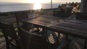 A wooden deck with a table and chairs overlooking a body of water during sunset. - MacEachern 19th Hole Celtic House (Creignish)