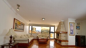 A spacious living room with wooden flooring, a fireplace, and a large window offering a city view. - Exc PH, Best Loc, Near Carolina, Huge Balcony, AMZ Views, WiFi, APU, 💲Deals! (Quito Canton)