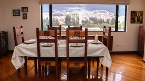 A dining area with a table set for six, wooden chairs, and a large window offering a city view. - Exc PH, Best Loc, Near Carolina, Huge Balcony, AMZ Views, WiFi, APU, 💲Deals! (Quito Canton)