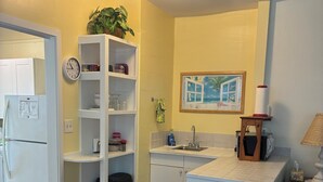 Una cocina compacta con armarios blancos, un lavamanos, un reloj y una planta en maceta.