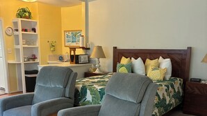 Un dormitorio con dos sillones grises, una cama con cubrecama de camuflaje, un cabecero de madera y una mesita de noche con lámpara.