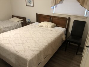 A bedroom with two beds, a nightstand, a chair, and a window with curtains. - Summer getaway.  Right on the water.  3 bedrooms pets permitted. (Milton)
