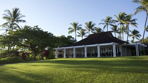 A covered outdoor seating area with tables and chairs, surrounded by a well-maintained lawn and palm trees. - Enjoy a Hawaiian vacation in Paradise Stay @ The World Famous Mauna Lani Resort (Puako)