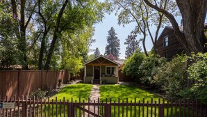 A wooden house with a front porch, surrounded by a wooden fence and lush greenery.