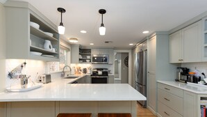 A modern kitchen with white countertops, stainless steel appliances, and wooden bar stools.