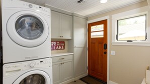 A laundry room with stacked washers and dryers, wooden cabinets, a door with a window, and a welcome sign.