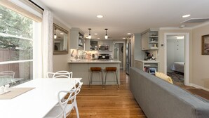 A modern kitchen with white cabinetry, a dining area with a white table and chairs, and a grey sofa in the living area.