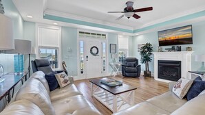 A spacious living room with a sofa set, a coffee table, a fireplace, and a ceiling fan. - Magnificent 6br/6bth home w/ IN-GROUND HEATED POOL & Luggage Lift! (Edisto Island)