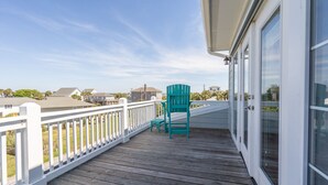 A wooden deck with a white railing, a teal chair, and a glass door. - Magnificent 6br/6bth home w/ IN-GROUND HEATED POOL & Luggage Lift! (Edisto Island)