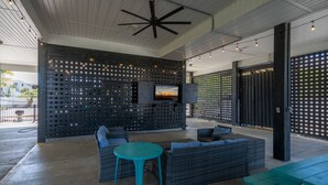 A covered outdoor seating area with wicker furniture, a television mounted on a wall, and string lights. - Magnificent 6br/6bth home w/ IN-GROUND HEATED POOL & Luggage Lift! (Edisto Island)